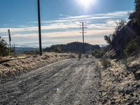 a dirt road through an empty mountain side with telephone poles next to it on a sunny day