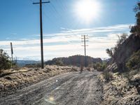 a dirt road through an empty mountain side with telephone poles next to it on a sunny day