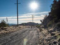 a dirt road through an empty mountain side with telephone poles next to it on a sunny day