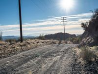 a dirt road through an empty mountain side with telephone poles next to it on a sunny day