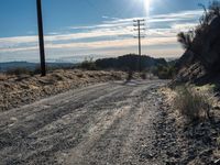 a dirt road through an empty mountain side with telephone poles next to it on a sunny day