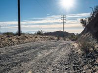 a dirt road through an empty mountain side with telephone poles next to it on a sunny day