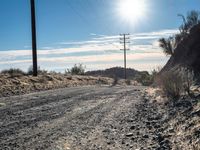 a dirt road through an empty mountain side with telephone poles next to it on a sunny day