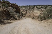 the dirt road leads to the hills and a steep cliff area in the background is covered with rocks