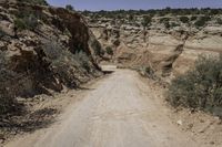 the dirt road leads to the hills and a steep cliff area in the background is covered with rocks