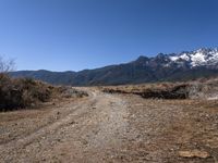 a wide dirt road leading through a scenic area of mountains and snow - capped peaks