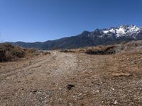 a wide dirt road leading through a scenic area of mountains and snow - capped peaks