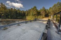 a dirt road by trees on a sunny day with benches next to it and two people