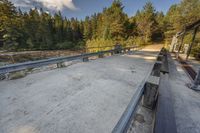 a dirt road by trees on a sunny day with benches next to it and two people