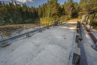 a dirt road by trees on a sunny day with benches next to it and two people