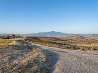 dirt road winding through an empty field towards a hill top and distant landscape with mountains in background