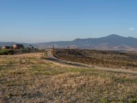 dirt road winding through an empty field towards a hill top and distant landscape with mountains in background