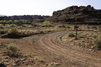 a dirt road is going through a desert landscape and mountains in the background, there are rocks and dry grass