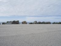 an empty parking lot near the ocean in california with one single plane flying overhead over the resturance