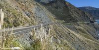 a truck on the road along the cliff side by the ocean and some mountains and water