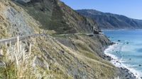 a truck on the road along the cliff side by the ocean and some mountains and water