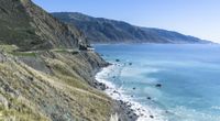 a truck on the road along the cliff side by the ocean and some mountains and water