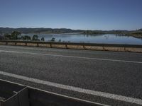 a car driving down the side of the road beside water with mountains in the distance