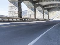 a person riding a bike underneath a bridge next to a mountain top, with some stone columns