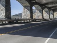 a person riding a bike underneath a bridge next to a mountain top, with some stone columns