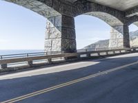 a person riding a bike underneath a bridge next to a mountain top, with some stone columns