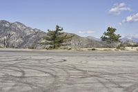 a view along a dirt road of an empty field and mountains in the distance of the scene