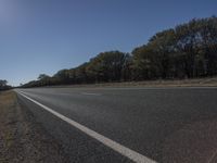 a car driving down the highway beside some trees and grass in the foreground with some sun shining