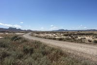 an empty road in a wide open plain of land near mountains and water on a sunny day