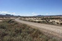 an empty road in a wide open plain of land near mountains and water on a sunny day