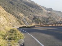 a highway winding through the hills near trees and grass near mountains with cars driving on the side