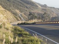 a highway winding through the hills near trees and grass near mountains with cars driving on the side