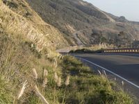 a highway winding through the hills near trees and grass near mountains with cars driving on the side