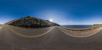 road in front of mountains and a sunny sky with sun and sunburst above them