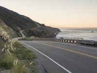 a beautiful view of a ocean, road and mountains with waves in the distance,