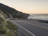 a beautiful view of a ocean, road and mountains with waves in the distance,