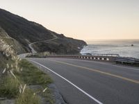 a beautiful view of a ocean, road and mountains with waves in the distance,