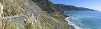 a car is driving down a steep road by the ocean in a valley on the island