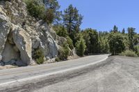 a long empty mountain road by a rock cliff, with trees and a blue sky in the background