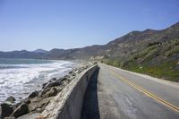 a paved mountain road next to the ocean on a sunny day with a car on it