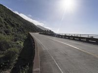 a car driving down a scenic freeway surrounded by hills and ocean shore cliffs on a sunny day