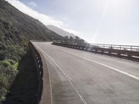 a car driving down a scenic freeway surrounded by hills and ocean shore cliffs on a sunny day