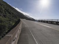 a car driving down a scenic freeway surrounded by hills and ocean shore cliffs on a sunny day