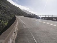 a car driving down a scenic freeway surrounded by hills and ocean shore cliffs on a sunny day