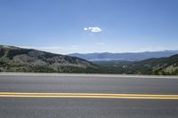 two yellow lines on the road with trees and mountains in the distance, in front of a clear sky