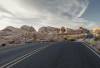 a view down a winding mountain road, in the desert at sunset time with a few clouds