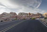 a view down a winding mountain road, in the desert at sunset time with a few clouds