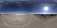 a fish eye lens shot of a desert area with a sun in the distance and dark clouds in the sky