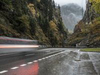 a car is driving down an empty highway during the rain and foggy morning, with mountain in the background