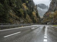 a car is driving down an empty highway during the rain and foggy morning, with mountain in the background
