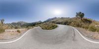 a curved road and hills with sun coming up on the mountain side, in a 360 - view camera